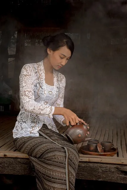 Femme balinaise en kebaya et sarong versant le thé dans des tasses en terre cuite