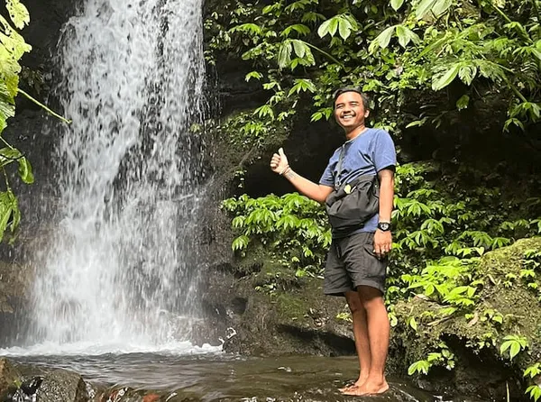 Komang, guide à Bali, souriant devant une cascade tropicale